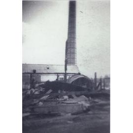 Demolished condensery building with brick chimney standing behind
